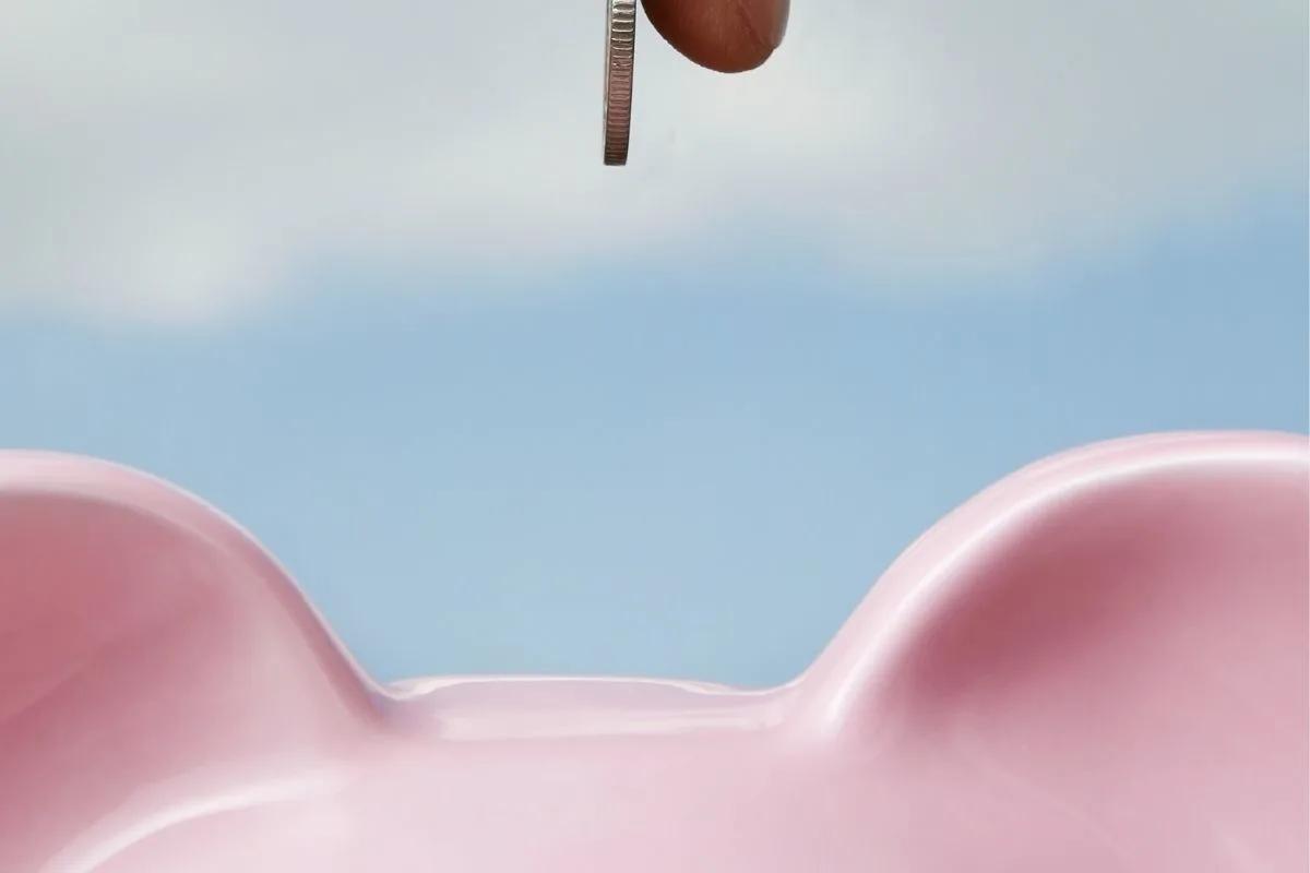 Blue background with someone putting a coin in a pink piggy bank