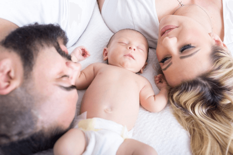 Two parents laying next to a baby