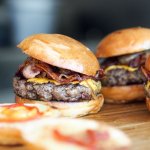 Four beef burgers sat on a woodern board