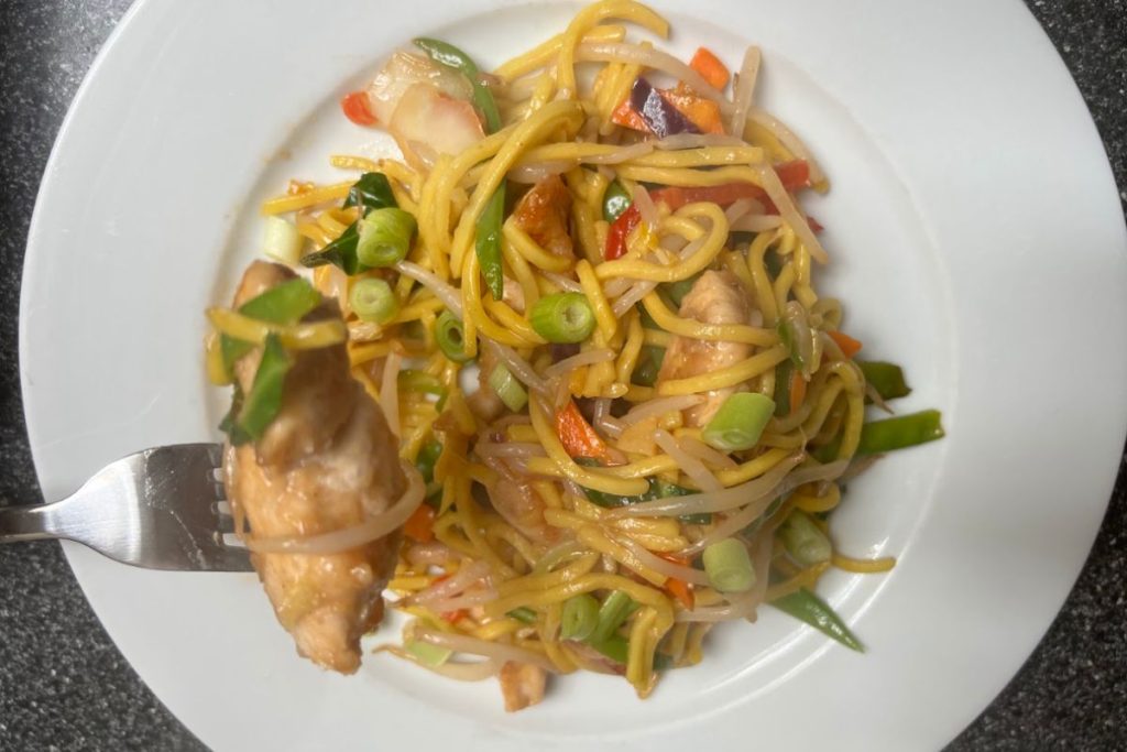 Chicken with noodles and vegetables on a white plate.