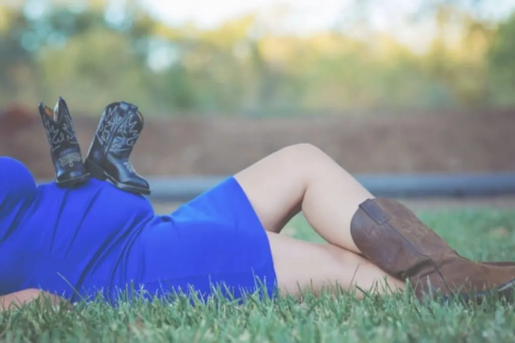 Woman laying in the grass with baby boots on her belly