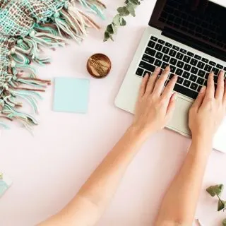 Lady typing on a laptop with a pink background